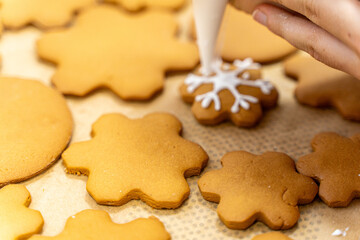 A pastry chef hand with a cooking bag decorates cookies in the form of a snowflake. Gingerbread, New Year or Christmas cookie decor.