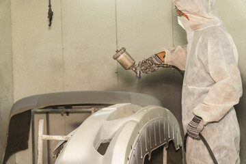 Professional painter applying white coating on car body panel in a spray booth during daytime