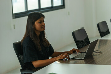Professional woman working on laptop in modern office setting with bright natural light