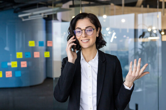 Confident businesswoman talking on phone in office, gesturing expressively. She exudes professionalism and clarity in communication, embodying modern business etiquette.