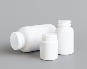 White plastic pill bottles closeup against grey, mockup. Healthcare concept, herbal supplements