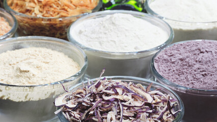A bowl of flour is next to a bowl of rice. There are several bowls of different ingredients, including flour, rice, and other grains