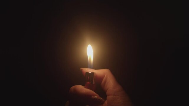 Woman's hand with a gas lighter. A woman kindles a fire. light fire gas lighter in the dark. a lighter flame on a black background. ignited by sparks. The lighter.