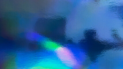 Abstract Holographic Background with Rainbow Colors and Shiny Particles on the dark blue background. The texture of foil paper is blurred, creating an effect of light refraction.