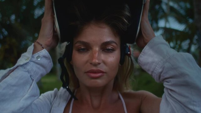 Sexy girl in the tropics puts off a retro motorcycle helmet. Beautiful woman in Asia puts off an old-fashioned hard hat. Blonde female enjoys a vacation in bali indonesia. Red swimsuit, palm tree
