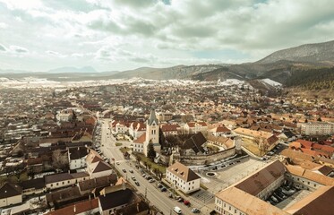 Glimpses of snow-dusted rooftops and winding streets fill the landscape of Brasov, Romania. The majestic Piatra Craiului Mountains rise in the background, surrounding the charming town of Rasnov