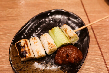 close up of grilled Japanese mushroom and welsh onion skewer on a black plate