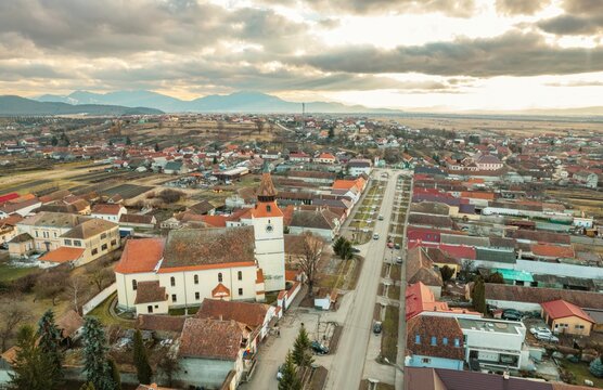 Breathtaking aerial view of Rasnov showcasing quaint rooftops, the historic church, and the stunning backdrop of Piatra Craiului mountains during a serene evening