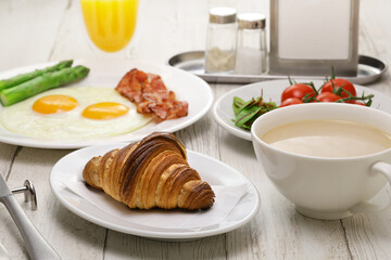 breakfast with croissant, cafe au lait, orange juice, fried eggs, bacons and vegetables.