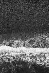 A black and white photo of the ocean with a wave. The water is choppy and the sky is dark