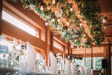 A large, long, decorated, wooden table and chairs, covered with a white tablecloth with dishes, flowers, candles, stands outdoor near the forest in nature. Wedding banquet. lights on background