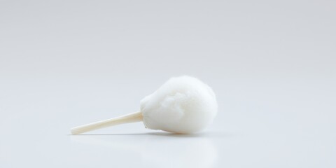 Fototapeta premium A single cotton swab lays on a white background with its soft, fluffy tip pointing towards the right