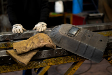 gloves and protective mask for a welder whose hands come out of the background with an iron