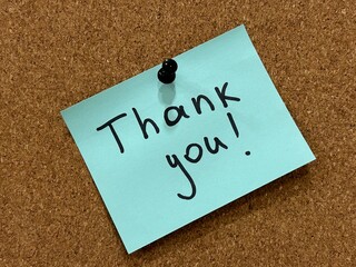 Handwritten Thank you on a memo note isolated on a cork board background. Gratitude concept