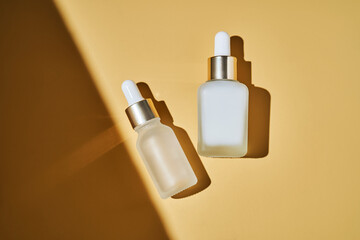 Two bottles of serum on a beige background with a beautiful shadow.