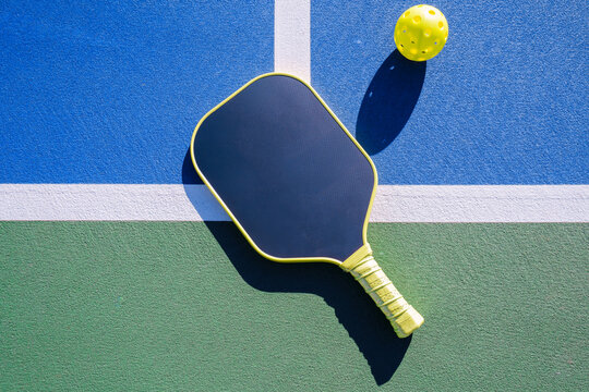 High-angle view of pickleball paddle and ball on court surface