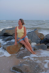 woman on the beach woman sits and walks on the seashore with a hat in summer autumn spring looks at the area water sky European appearance there are emotions on the face in shorts and a T-shirt beauti
