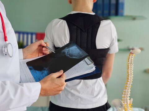 Healthcare professional is reviewing an x-ray report while standing behind a patient who wears a back brace concept