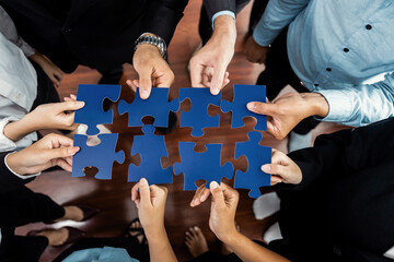 Top view multiethnic business people holding jigsaw pieces and merge them together as effective...