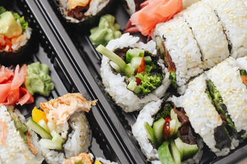 Sushi assortment in a black takeaway box. Closeup of California rolls, futomaki, and uramaki. Fresh Japanese cuisine with sesame seeds and colorful toppings. Lunch or dinner sushi to-go option.