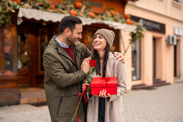 Fototapeta premium Caucasian man lovingly presents a gift to his wife during Valentine's Day in an urban setting.