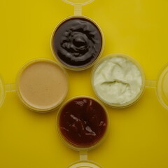 Four different sauces in jars for seasoning meat on a yellow background. Mayonnaise, ketchup, sauce.