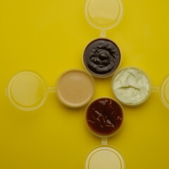 Four different sauces in jars for seasoning meat on a yellow background. Mayonnaise, ketchup, sauce.