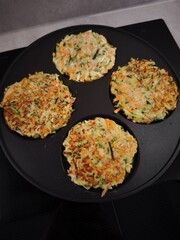 Delicious zucchini and carrot pancakes grilling on a modern frying pan