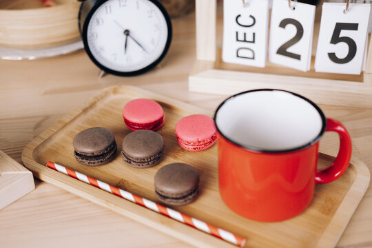 red mug with coffee and macaroons on a wooden tray on the background of an alarm clock and a calendar with the date December 25. Christmas coffee - Powered by Adobe