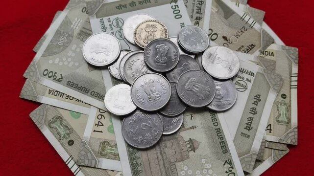 Pile of indian five hundred rupees (INR) currency notes or banknotes with scattered coins isolated on table background. India tax, bank deposit, loan and inflation concept. Closeup rotating top view.