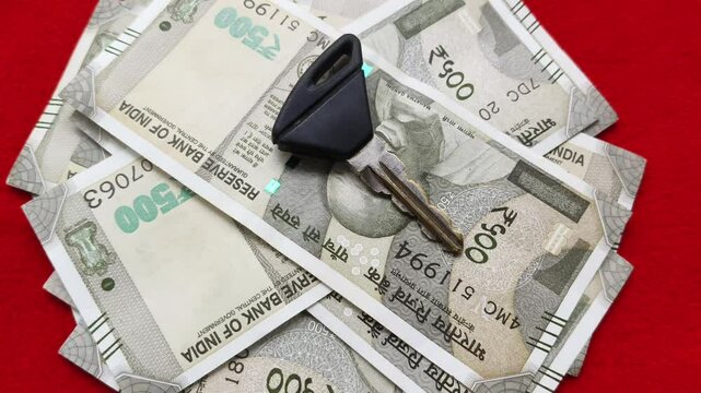 New motor bike vehicle metal key isolated on top of five hundred rupee indian currency notes. Bike loan monthly emi payment or rent expense concept. Extreme closeup macro rotating top view.