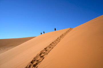 A group of tourists hiking on a dune ridge with footprints in the sand to reach the summit of Big...
