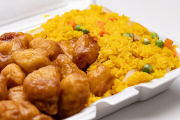 Chinese takeout in a white foam container featuring honey mustard deep-fried chicken bites paired with yellow fried rice mixed with vegetables like peas, carrots, and onions.
