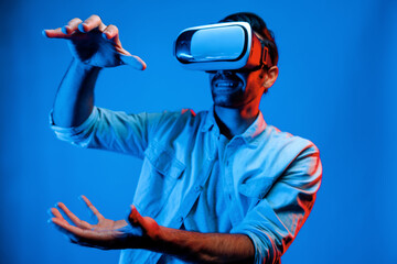 Caucasian smart man holding and moving gesture while using VR goggle. Happy person using headset and goggle while enter virtual world or metaverse with neon light background. Technology. Deviation.