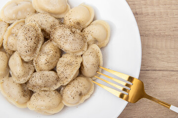 Boiled dumplings with spices in a plate. Golden fork