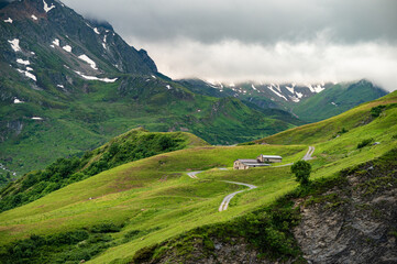 LES CHAPIEUX , Alps, France, Tour du Mont Blanc - the mountain shelter and farm near Cormet de Roselend  with high peaks in background and a winding road
