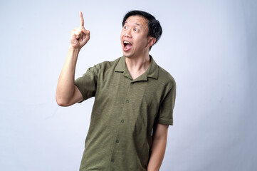 An Asian man in a casual green shirt excitedly points upward with one finger, mouth open in...