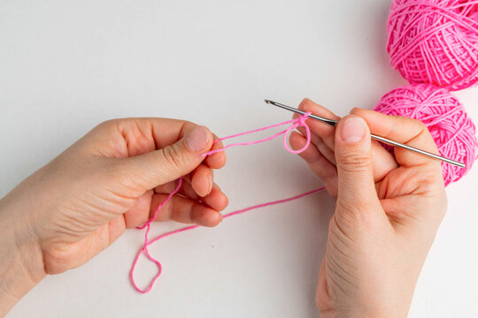 Hand holding thread of pink yarn and a chrocket hook on light background. Tutorial on how to crochet magic ring, step 6