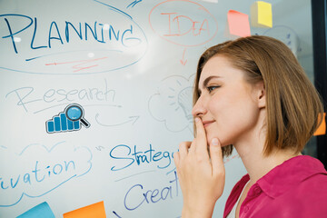 Young beautiful businesswoman putting sticker on glass board while finding a solution to solve...