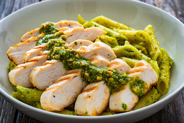 Penne with basil pesto sauce and grilled chicken breast on wooden table	