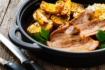 Tasty roast ribs with baked potatoes and sauerkraut salad in frying pan on wooden table