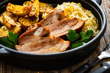 Tasty roast ribs with baked potatoes and sauerkraut salad in frying pan on wooden table