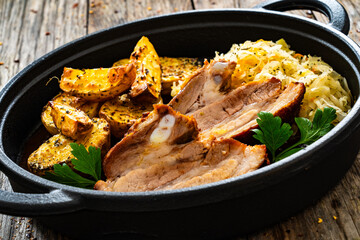 Tasty roast ribs with baked potatoes and sauerkraut salad in frying pan on wooden table