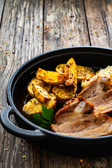 Tasty roast ribs with baked potatoes and sauerkraut salad in frying pan on wooden table