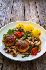 Fried pork meatballs with boiled potatoes and fried mushrooms on wooden table