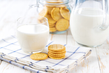 Glass and a jug of fresh milk with wheat crackers round shape on a white table, selective focus.