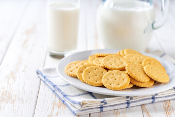 Glass and a jug of fresh milk with wheat crackers round shape on a white table, selective focus.
