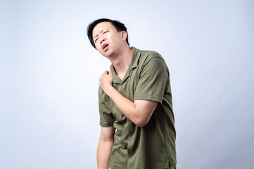 An Asian man in a casual green shirt holds his shoulder, showing discomfort or pain, against a...