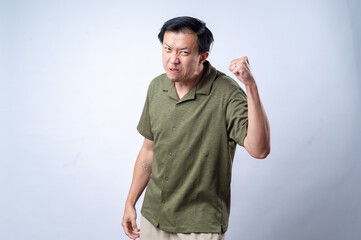 An Asian man in a green shirt shows anger and determination with a clenched fist raised and a fierce expression, conveying a sense of defiance or frustration, against a plain white background