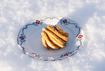 Knotted cinnamon roll pastry on a floral patterned plate in fresh winter snow
